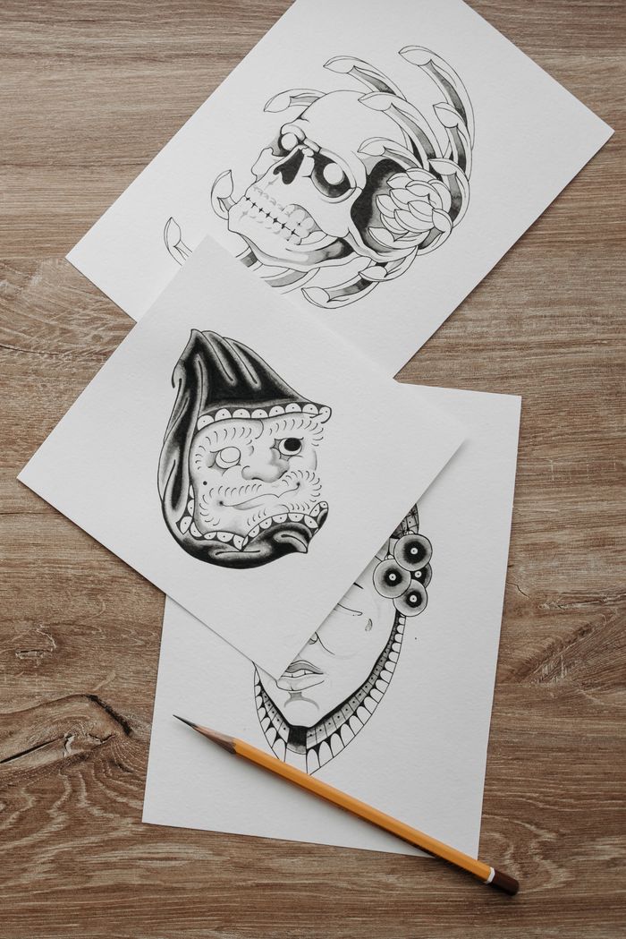 Detailed tattoo design sketches on paper with pencil on a wooden table. Perfect for artists and designers.